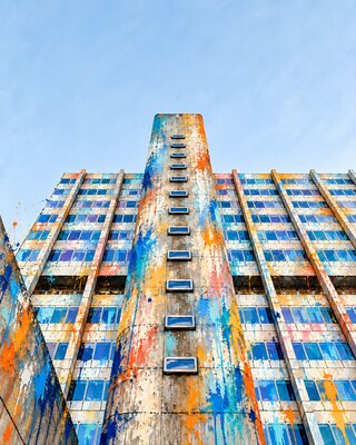 The same tower splashed with paint, blue, orange and red running down the concrete under a bright sky.