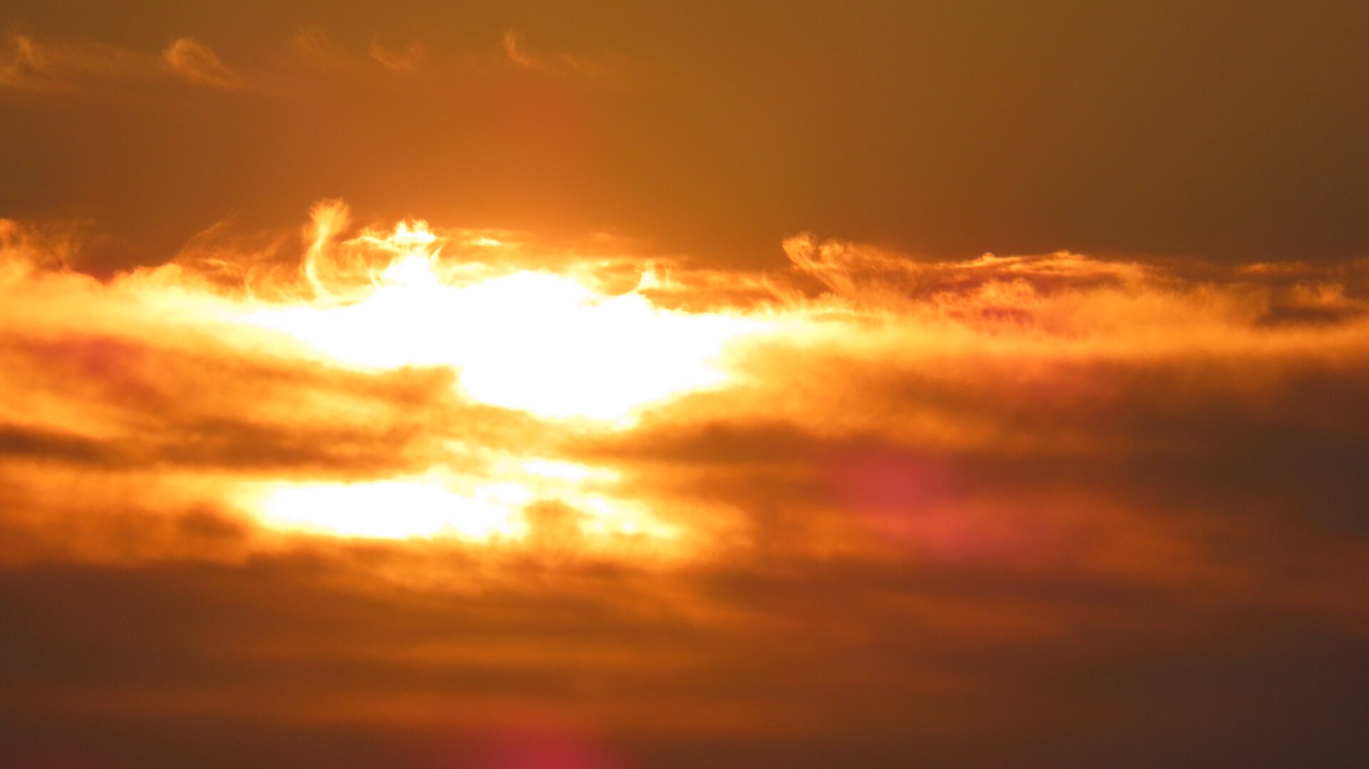 The sun going down behind a band of cloud, the whole sky in amber and orange.