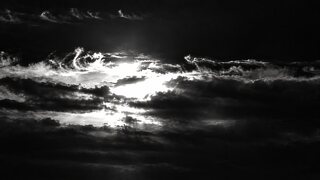 The same sunset in black and white, the clouds dark and the sun a white burn through them.